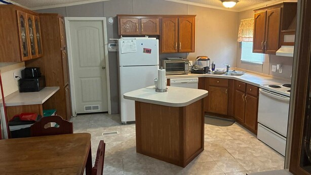 Una cocina compacta con armarios de madera, un refrigerador blanco, un microondas y una pequeña isla con pileta.