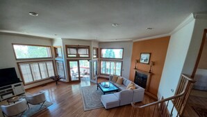 Amplia sala de estar con un sofá grande, una mesa de centro y una chimenea. Hay ventanas amplias y una escalera.