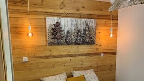 Un dormitorio con pared de madera, una cama con ropa de cama estampada, dos lámparas fijadas a la pared y un adorno en la pared.
