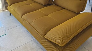 Un sofá amarillo tejido en una habitación con pared de piedra y ventanas amplias con vistas a un paisaje montañoso.