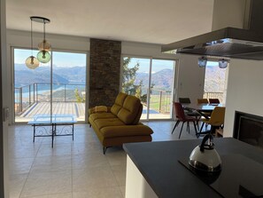 Un salon moderne comprenant un canapé, une table à manger et un coin cuisine, avec de grandes fenêtres offrant une vue sur les montagnes.