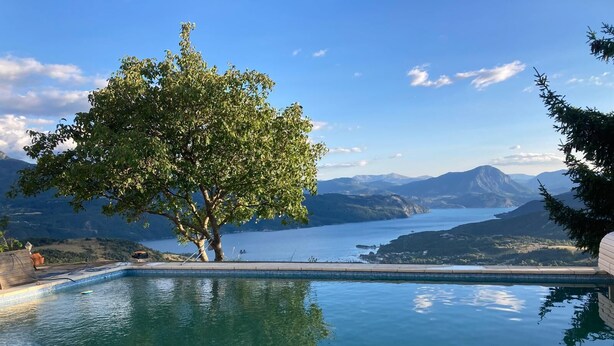 Una piscina con un árbol en primer plano y un paisaje montañoso al fondo.