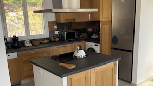 Una cocina moderna con armarios de madera, un refrigerador de acero inoxidable, un microondas y un hervidor en la isla.