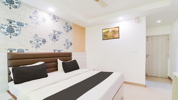 A bedroom with a large bed, a headboard, a ceiling fan, a wall with a floral pattern, and a door. - Premium Civil Lines Near Old Bus Stand (Bareilly)