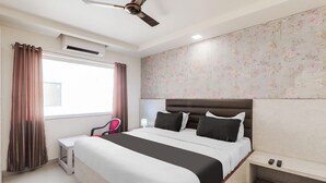 A hotel room with a bed, a bedside table, a chair, a ceiling fan, and a window with curtains. - Premium Civil Lines Near Old Bus Stand (Bareilly)