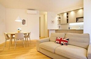 Ein modernes Wohnzimmer mit einer Couch, einem Esstisch mit Stühlen und einer Küchenzeile mit Schränken und Spüle.