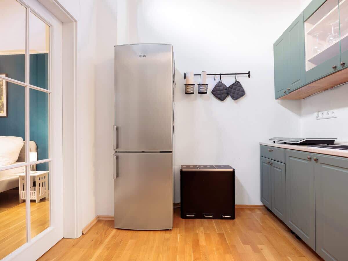 Una cocina compacta con un refrigerador de acero inoxidable, una encimera pequeña y un estante en la pared con utensilios de cocina.