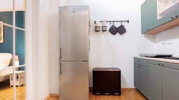 Una cocina compacta con un refrigerador de acero inoxidable, una encimera pequeña y un estante en la pared con utensilios de cocina.