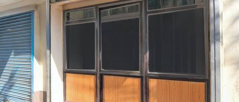A building facade with a large window with a black frame and wooden panels, a blue shutter door, and a concrete ground.