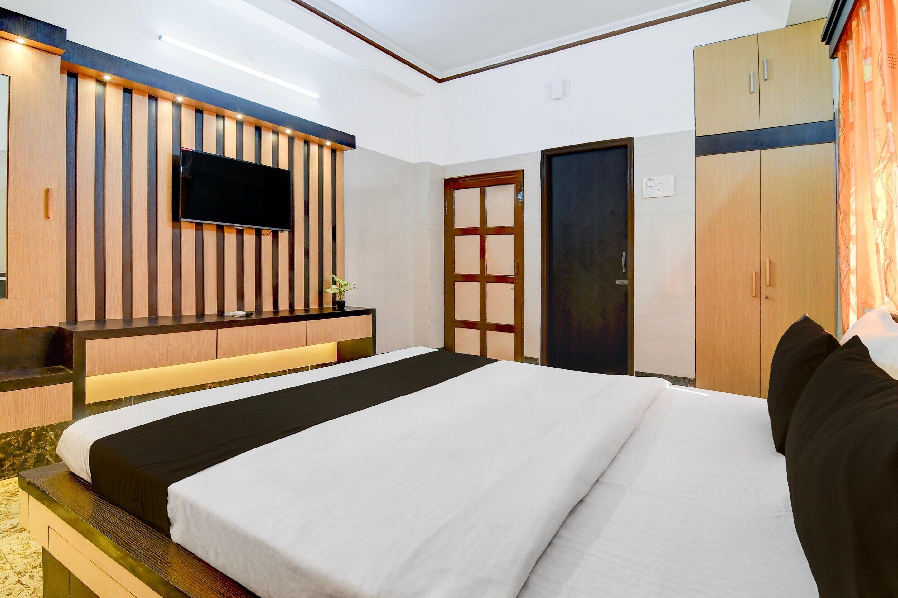 A hotel room with a bed, a TV mounted on the wall, a wardrobe, and a door.