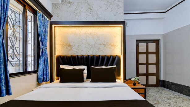 Une chambre d’hôtel dotée d’un grand lit, d’une tête de lit avec éclairage intégré, d’une table de chevet avec un vase et d’une porte au design traditionnel.