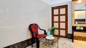 Un hall d’hôtel avec une table en verre, un fauteuil rouge, une porte en bois et un sol en marbre.