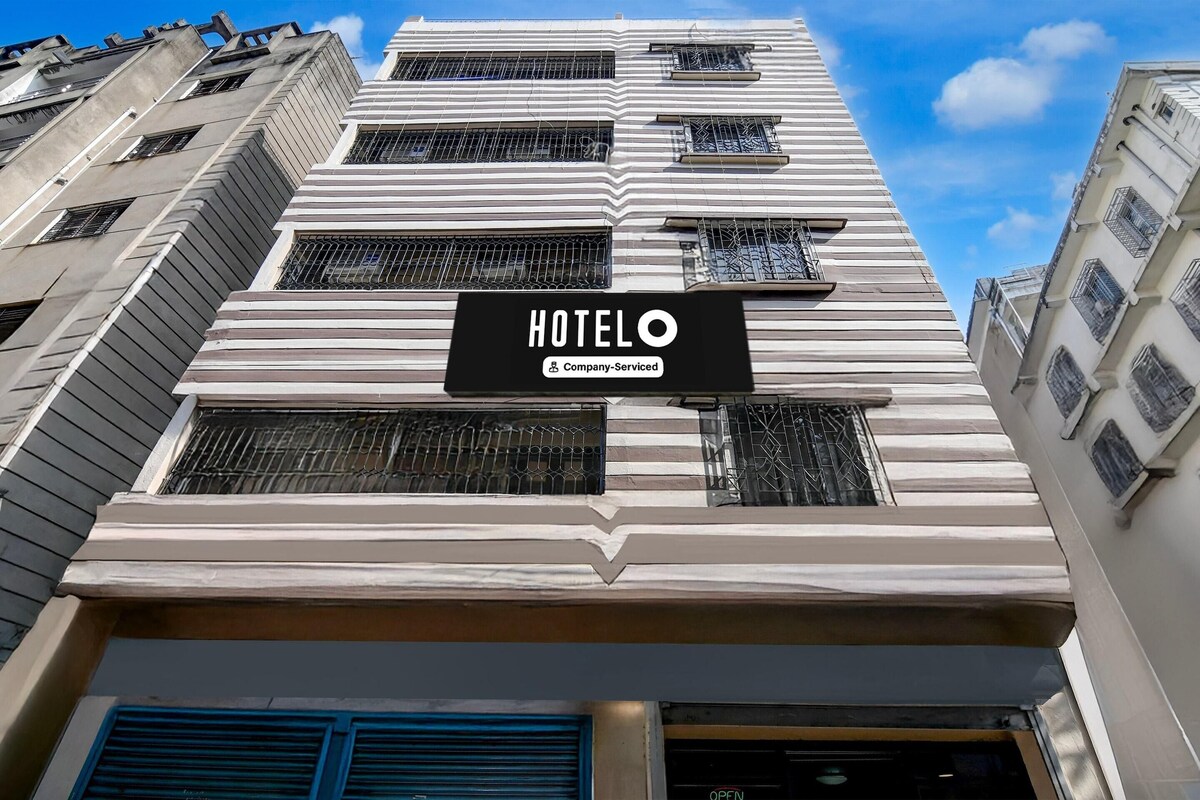 Edificio de hotel con letrero que indica servicio para empresa, múltiples ventanas con rejas de metal y un cielo azul despejado al fondo.