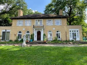 Une maison à deux étages, construite en briques, avec un porche à l’avant, une entrée centrale et un petit jardin.
