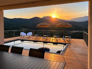 Piscina no terraço com espreguiçadeiras e guarda-sóis, com vista para uma paisagem montanhosa ao pôr do sol.