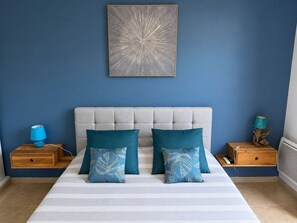Un dormitorio con una cama, dos mesitas de noche, una pared azul y una obra de arte enmarcada.