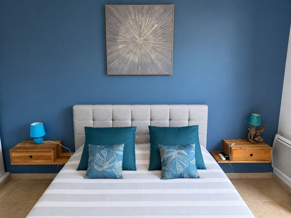 A bedroom with a bed, two nightstands, a blue wall, and a framed artwork.