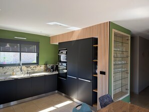 Una cocina moderna con armarios oscuros, horno empotrado y un armario con puerta de cristal y estantes.