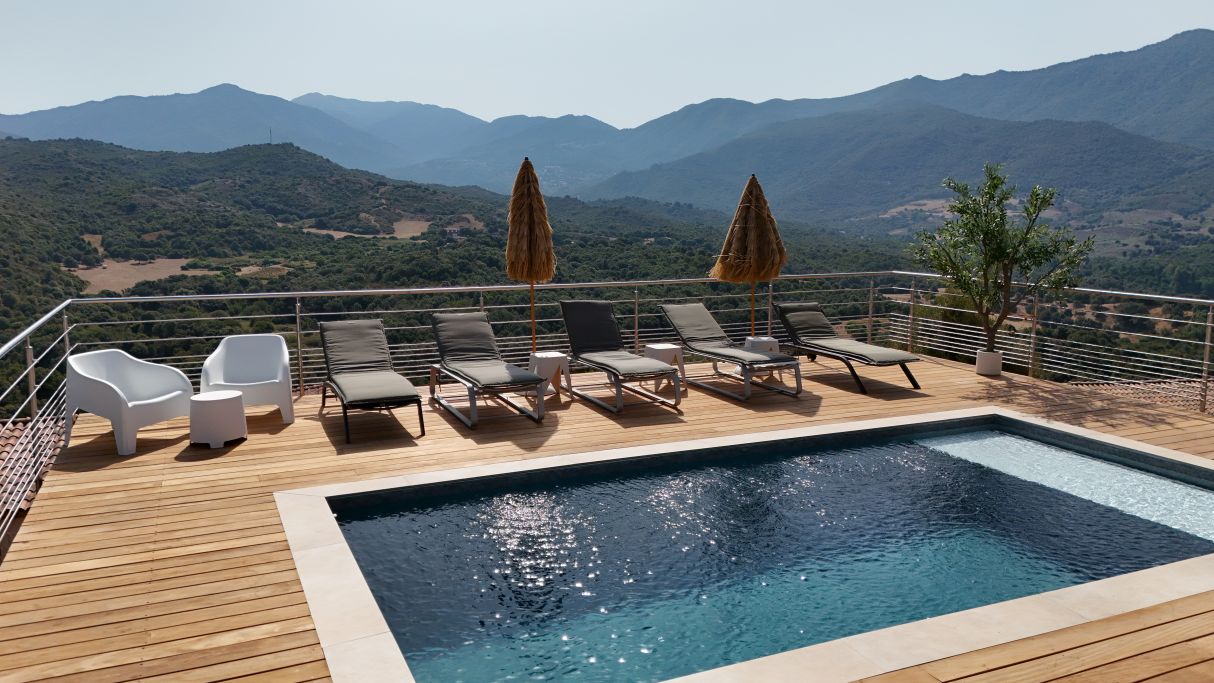 A poolside area with lounge chairs and umbrellas, overlooking a mountainous landscape.