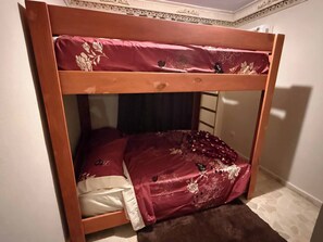 A bunk bed with a wooden frame, a lower bunk with a white mattress, and a top bunk with a red mattress.