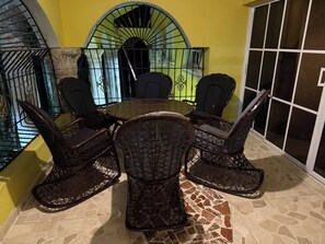 A dining area with a round table and six wicker chairs, a yellow wall, and a view of a staircase.