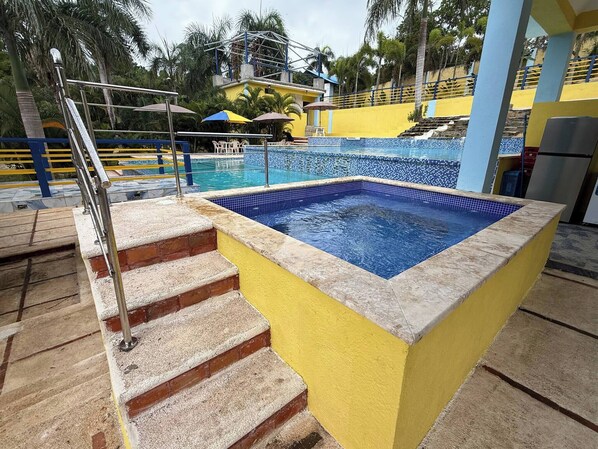 Una piscina con borde de azulejos, un conjunto de escaleras que la suben y una pared amarilla que rodea la zona de la piscina.