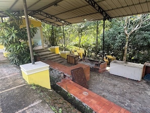 A covered outdoor area with steps leading to a yellow building, surrounded by greenery. - Segundo Piso Completó (Pedro Brand)