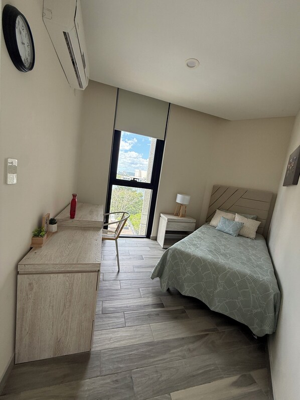 Une chambre de taille modeste, comprenant un lit, un petit bureau, une chaise, une table de chevet et une fenêtre donnant sur un paysage agréable.