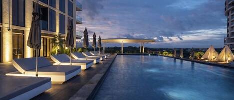 A poolside area with lounge chairs, umbrellas, and a building with large windows.