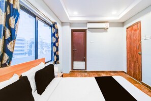 A hotel room with a bed, a window with curtains, an air conditioning unit, and a door. - Deluxethe Serene Woods Malkajgiri (Hyderabad)