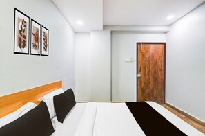 Ein Hotelzimmer mit einem Bett, einem Holz-Kopfteil, einer Tür und drei gerahmten Bildern an der Wand.