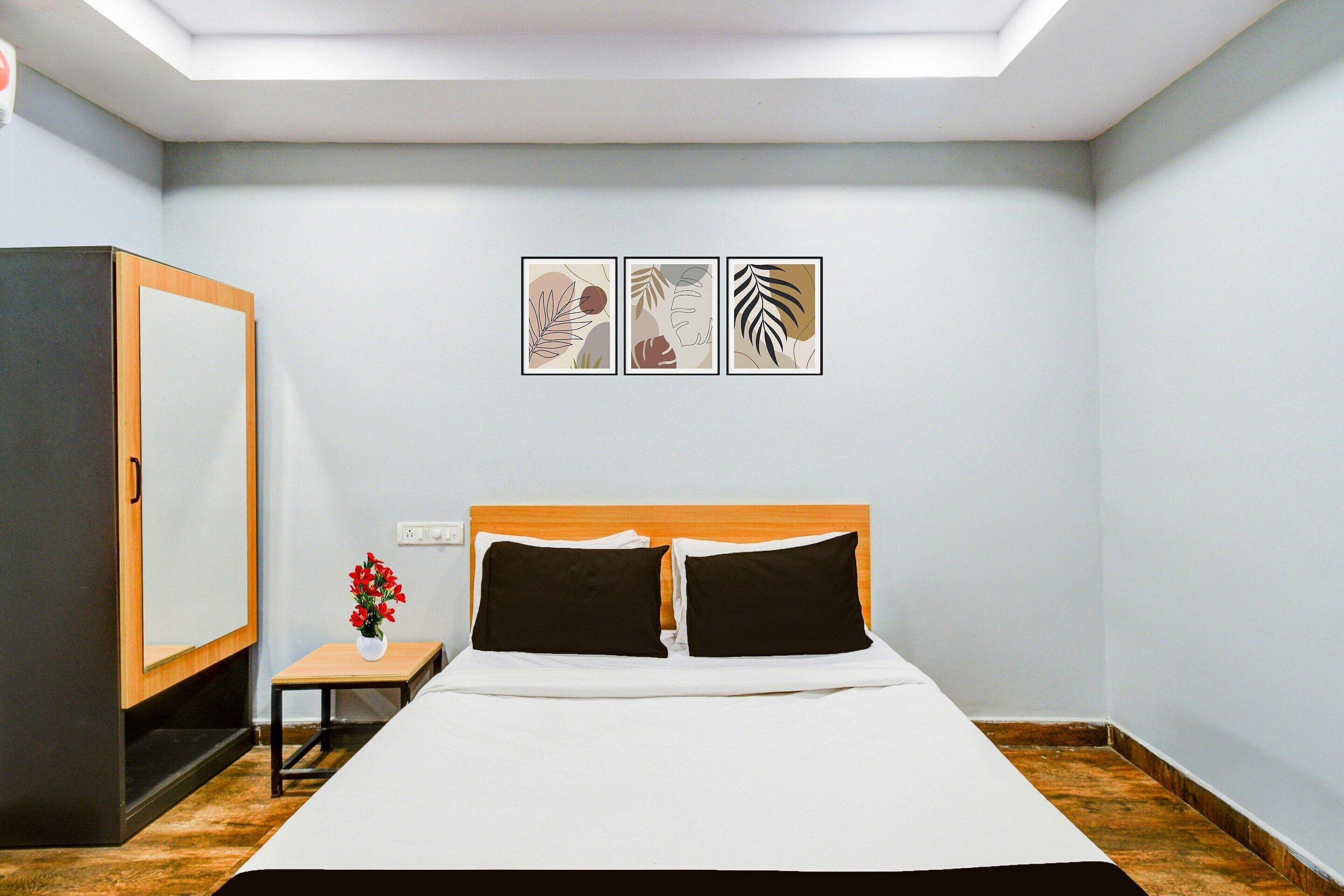 Un dormitorio con cama, mesita de noche, un florero con flores y tres cuadros en la pared.