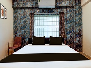A hotel room with a bed, a chair, a window, and patterned walls.