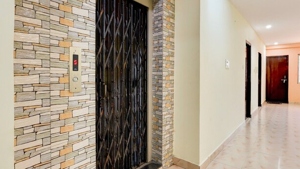 A hallway with a stone wall and a black door with a metal gate. - Deluxe Sai Nivas Rushikonda (Visakhapatnam)