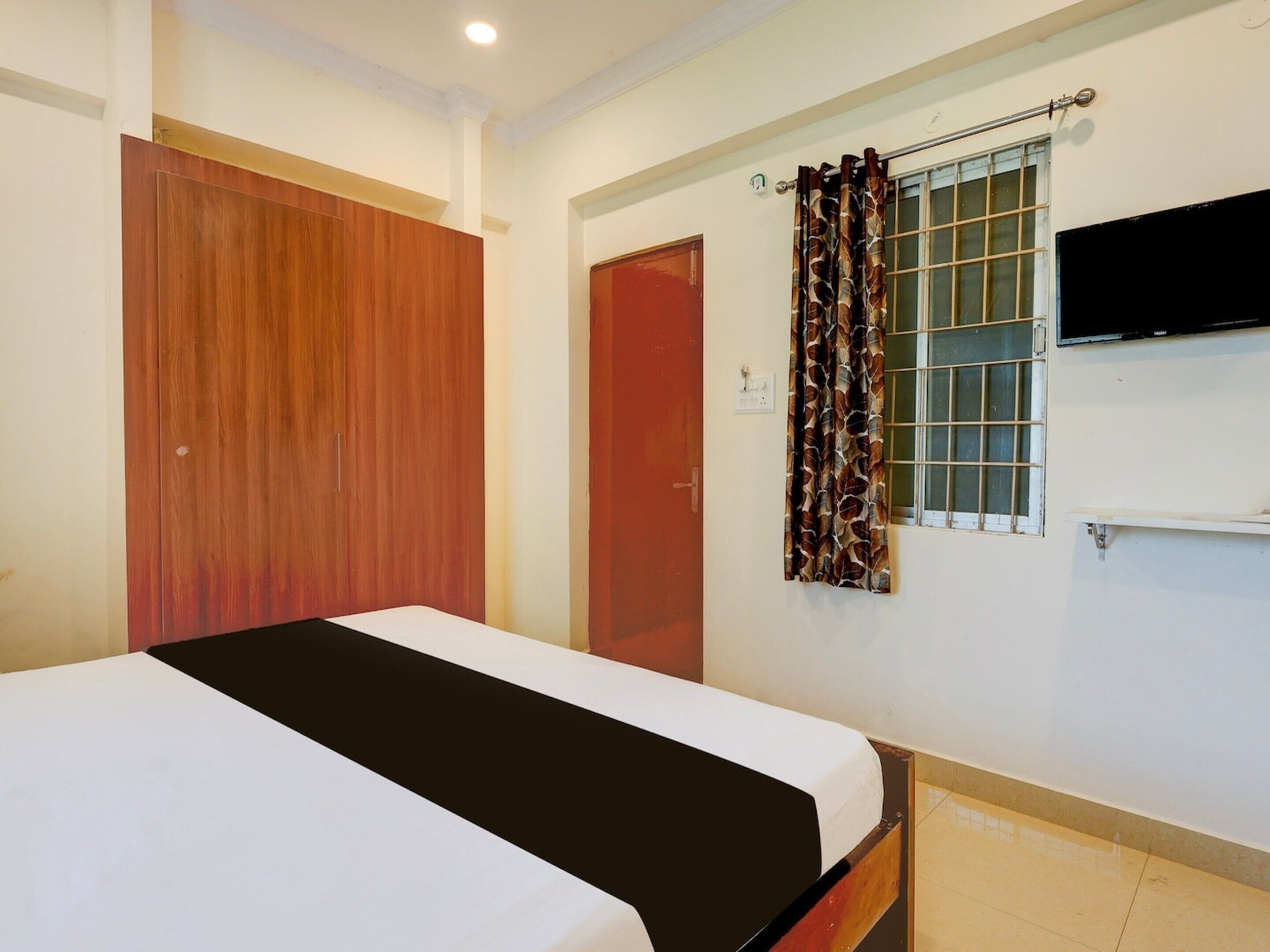 Un dormitorio con cama, armario, puerta, ventana con cortinas y televisión montada.