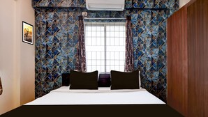 A hotel room with a bed, a window with curtains, a wall air conditioner, and a framed picture on the wall. - Deluxe Sai Nivas Rushikonda (Visakhapatnam)