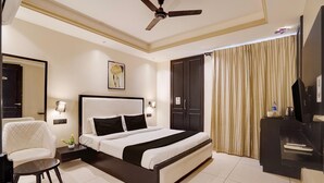 A hotel room with a bed, a chair, a desk, a television, and a ceiling fan. - Classic With Balcony Cloud Bay (Gurugram)