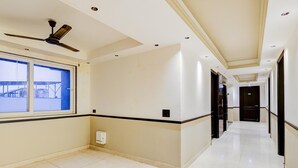 A hotel corridor with a ceiling fan, a window with a view, and a door at the end. - Classic With Balcony Cloud Bay (Gurugram)