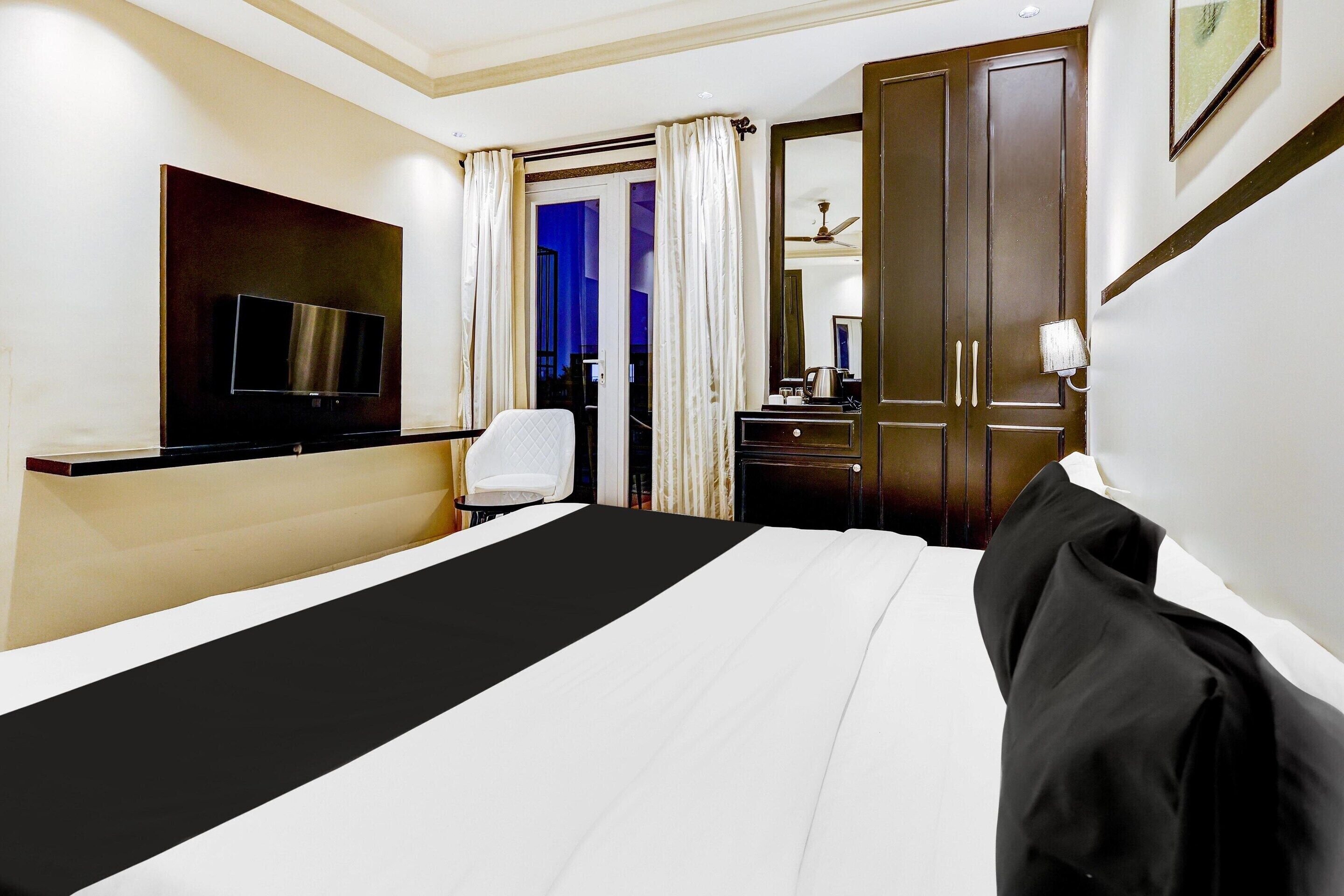 A hotel room with a bed, a TV, a desk, a chair, and a door leading to another room.