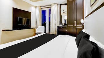 A hotel room with a bed, a TV, a desk, a chair, and a door leading to another room.