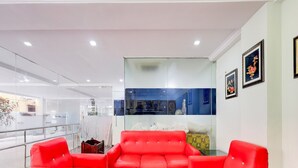 A modern interior with red sofas, a glass partition, and framed artwork on the walls. - Deluxe Benz Circle MG Road (Vijayawada)