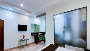 A hotel room with a bed, a desk, a chair, a TV, and a door. - Deluxe Benz Circle MG Road (Vijayawada)