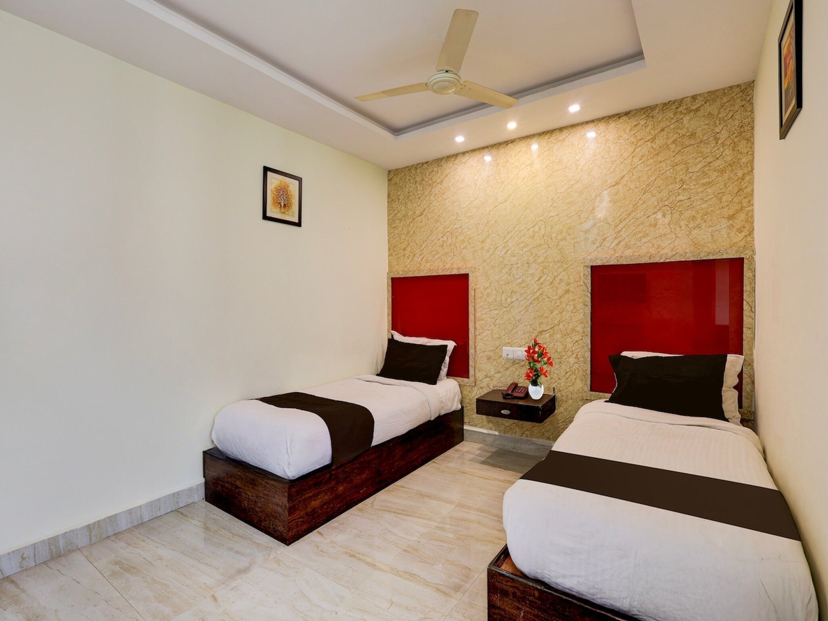 A hotel room with two beds, a ceiling fan, a marble wall, and a small table with a vase of flowers.
