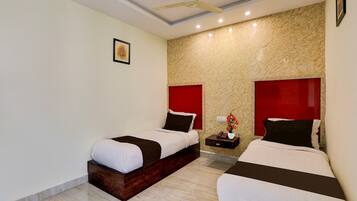 A hotel room with two beds, a ceiling fan, a marble wall, and a small table with a vase of flowers.
