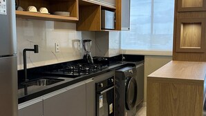 A modern kitchen with a built-in stove, sink, and washing machine, wooden cabinetry, and a large window. - Apto Metropolitan Novo na Ponta Negra (Manaus)