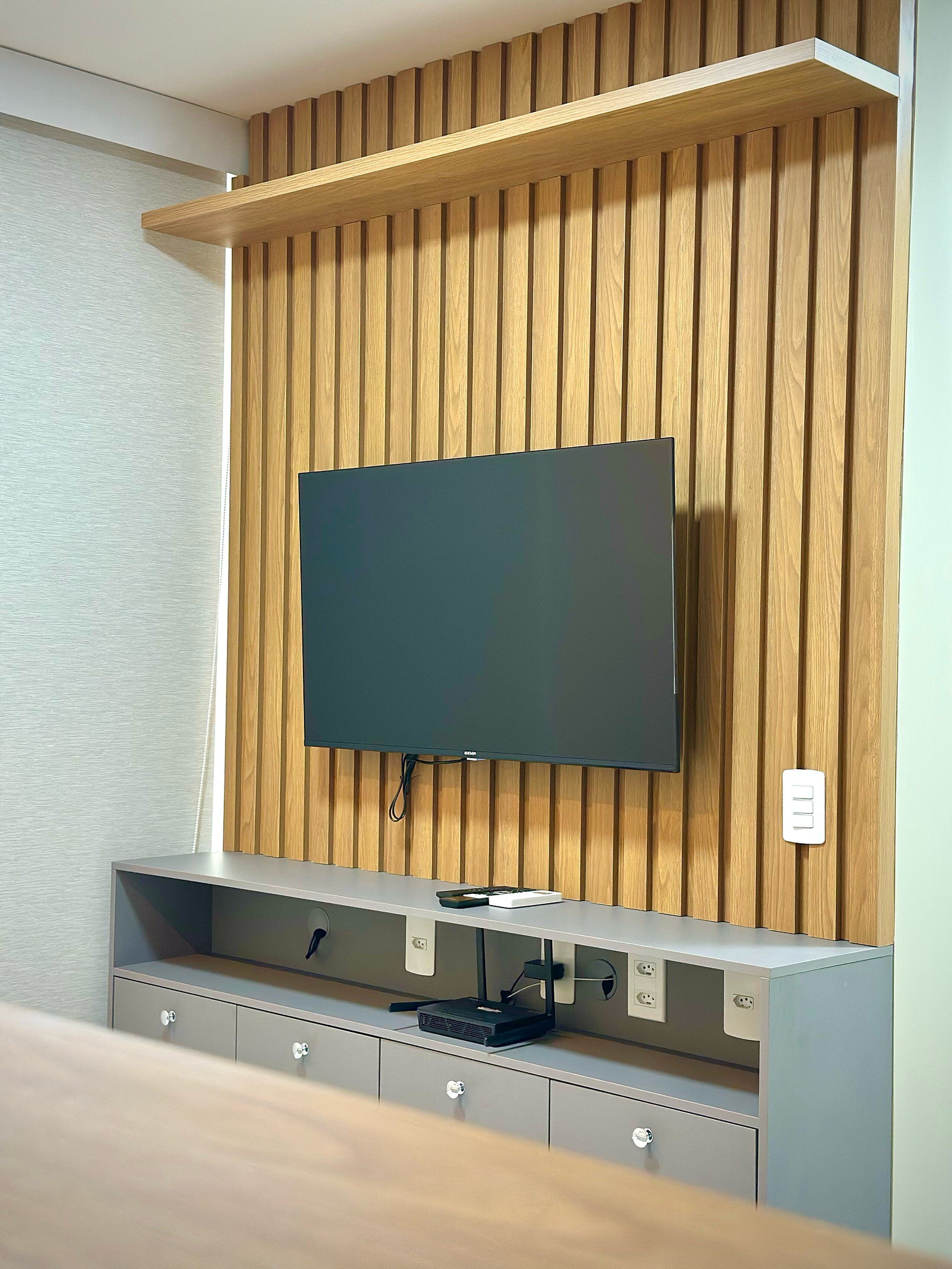 Un mueble moderno de entretenimiento con un televisor de pantalla plana montado en una pared de paneles de madera, un estante empotrado y una regleta con enchufes.