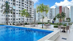 A swimming pool with lounge chairs and tables, surrounded by tall residential buildings. - Apto Metropolitan Novo na Ponta Negra (Manaus)
