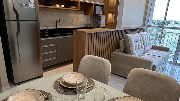 A modern kitchen with built-in appliances, a dining area set for four with a table and chairs, and a balcony with a view. - Apto Metropolitan Novo na Ponta Negra (Manaus)