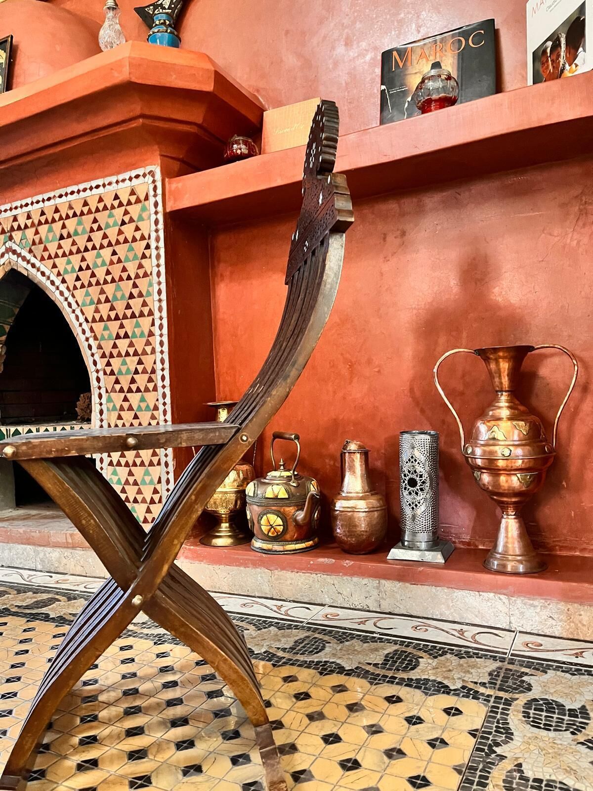 Un intérieur marocain traditionnel avec une chaise en bois, un sol carrelé et une étagère ornée d’objets décoratifs.