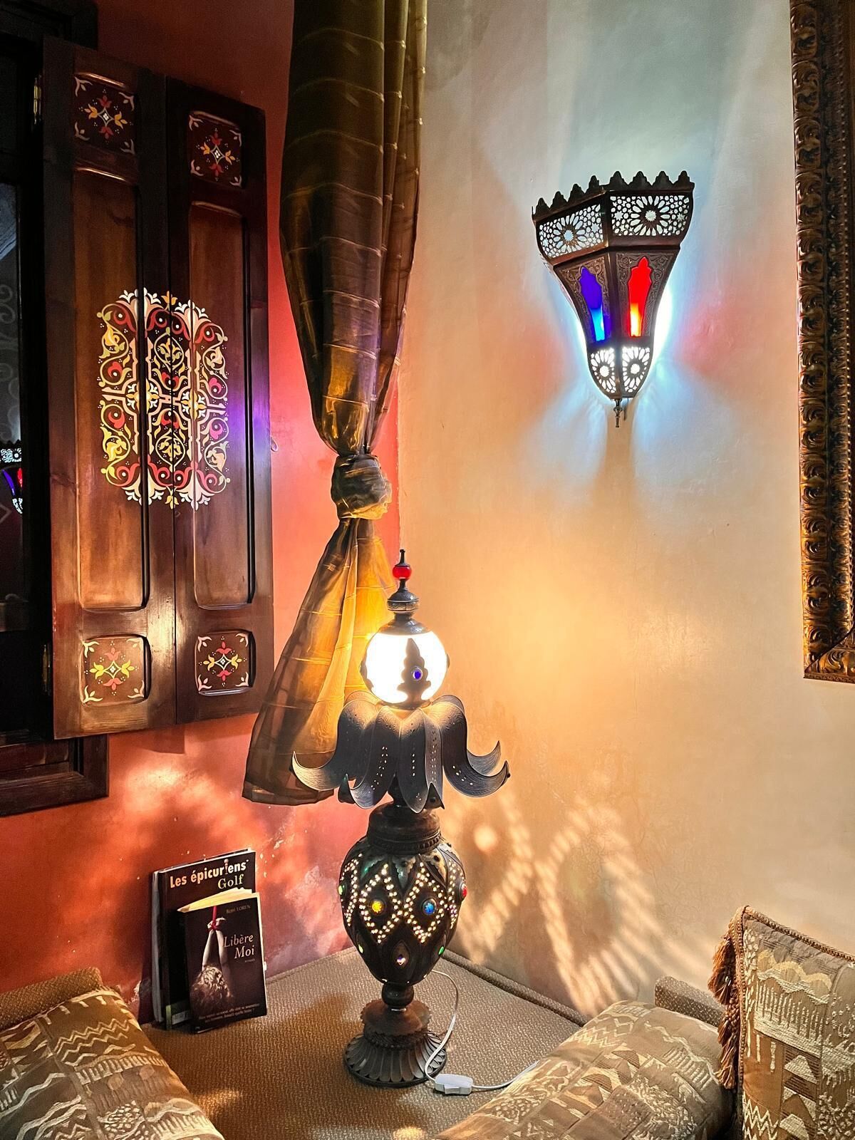 A room with a traditional lamp, a wall-mounted light fixture, and a book on a cushion.